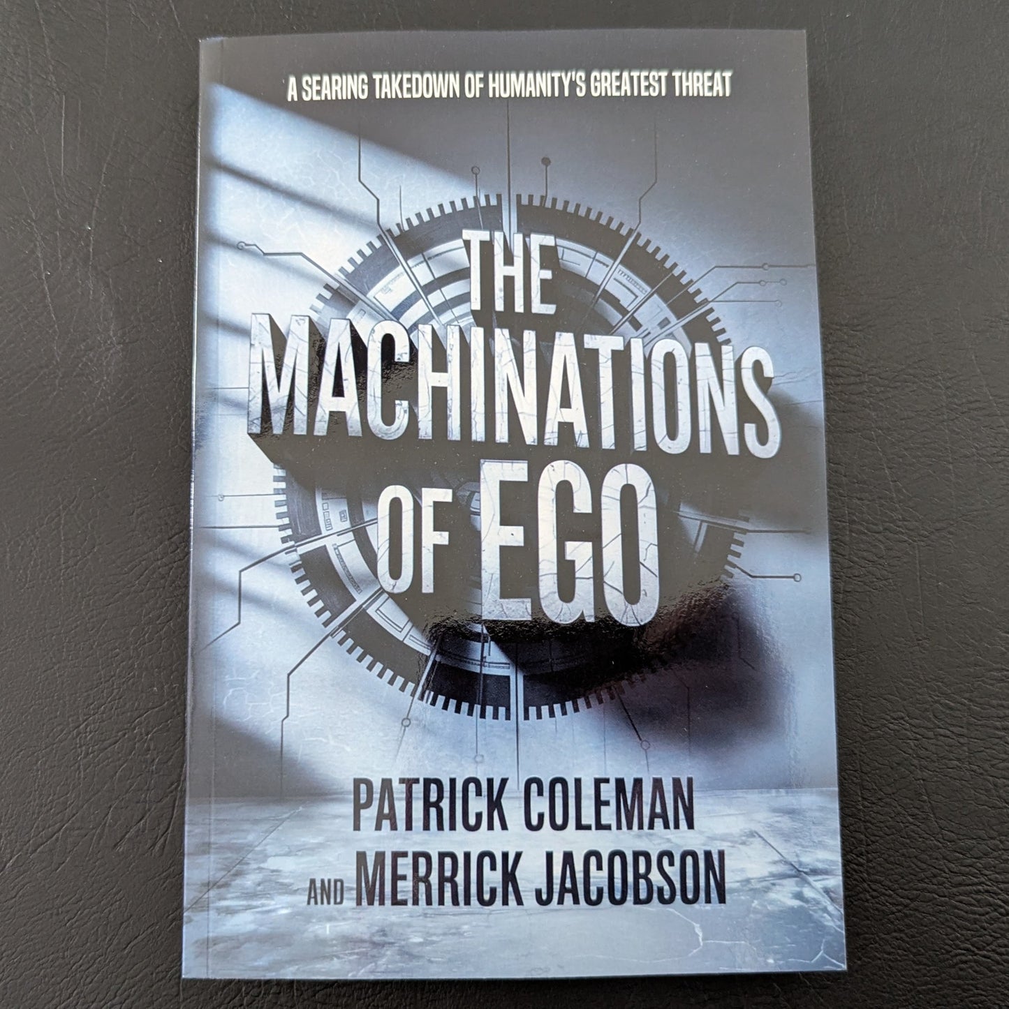 Book titled 'The Machinations of Ego' by Patrick Coleman and Merrick Jacobson on a dark surface