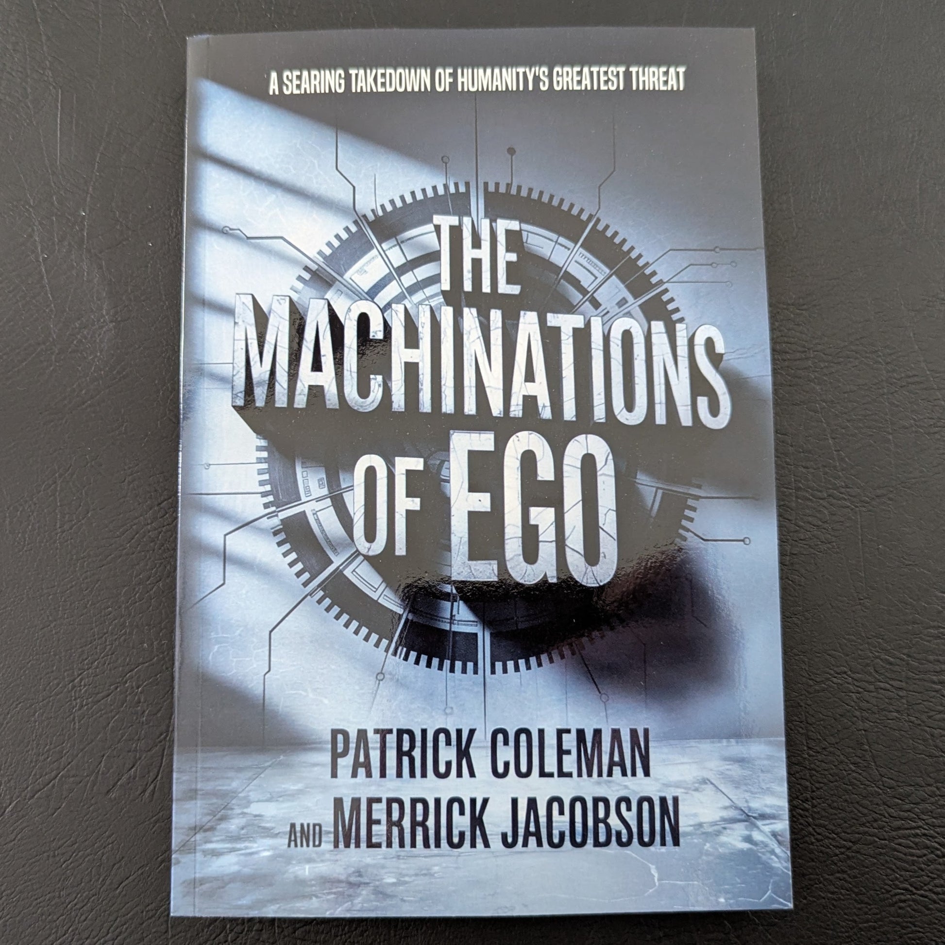 Book titled 'The Machinations of Ego' by Patrick Coleman and Merrick Jacobson on a dark surface